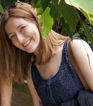 Photo of Natasha Simonova smiling to camera through the leaves of a tree.
