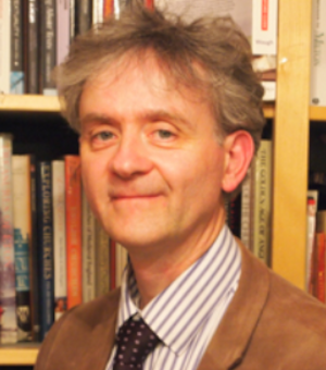 Photo of Richard Lawes looking to camera with a bookcase behind him.